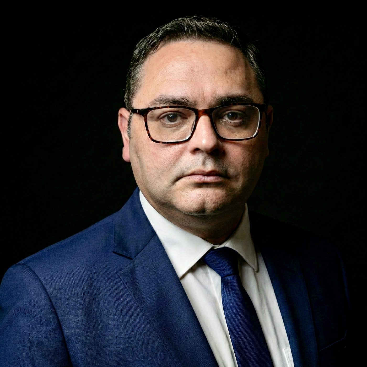 Dr. Roberto Rodrigues em retrato sóbrio, terno azul sobre fundo escuro